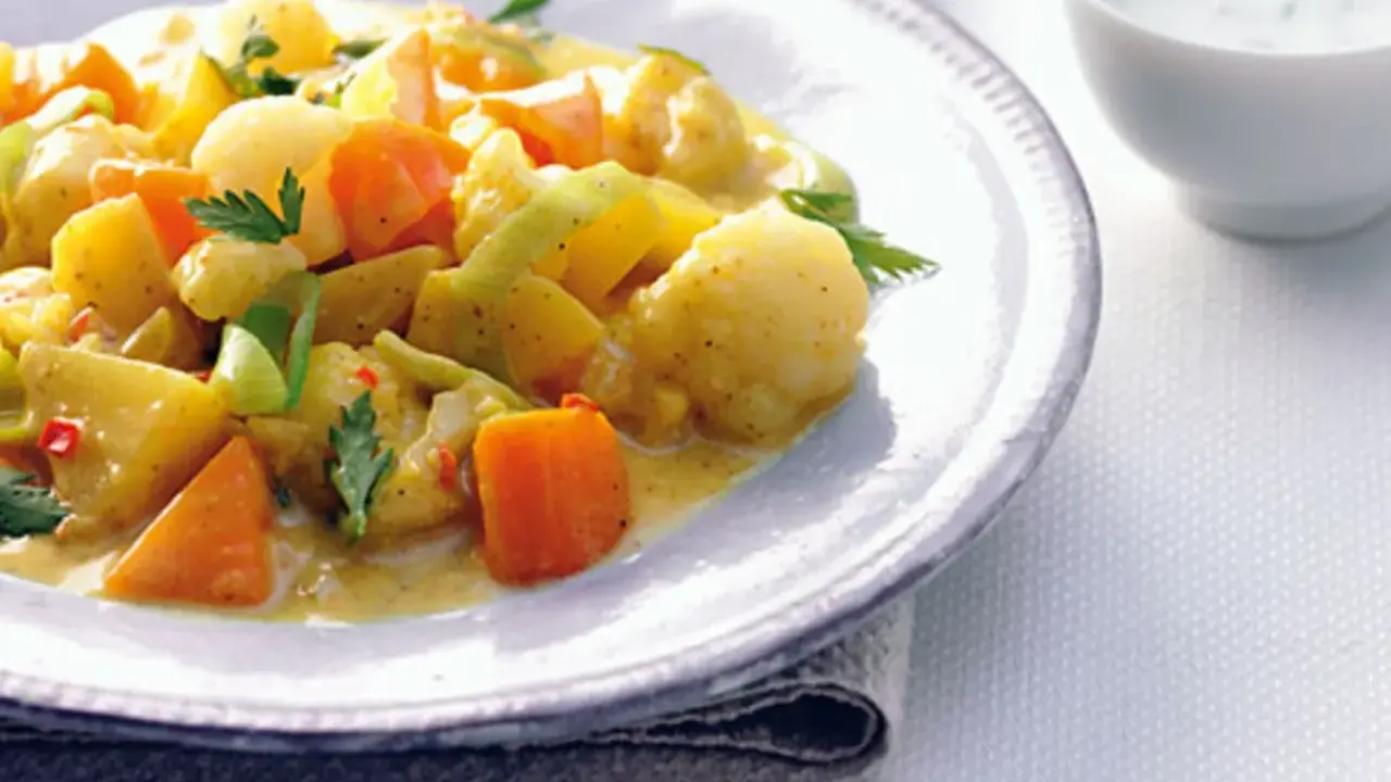 Ein Teller mit cremigem Curry-Eintopf, gefüllt mit Kartoffeln, Karotten und Lauch, garniert mit Petersilie.