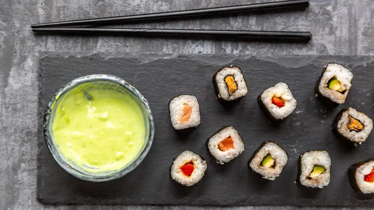 Sushi mit Lachs, Avocado und Paprika, dazu eine grüne Soße. Ist Wasabi gesund? Ja, es ist bekannt für seine entzündungshemmenden Eigenschaften.