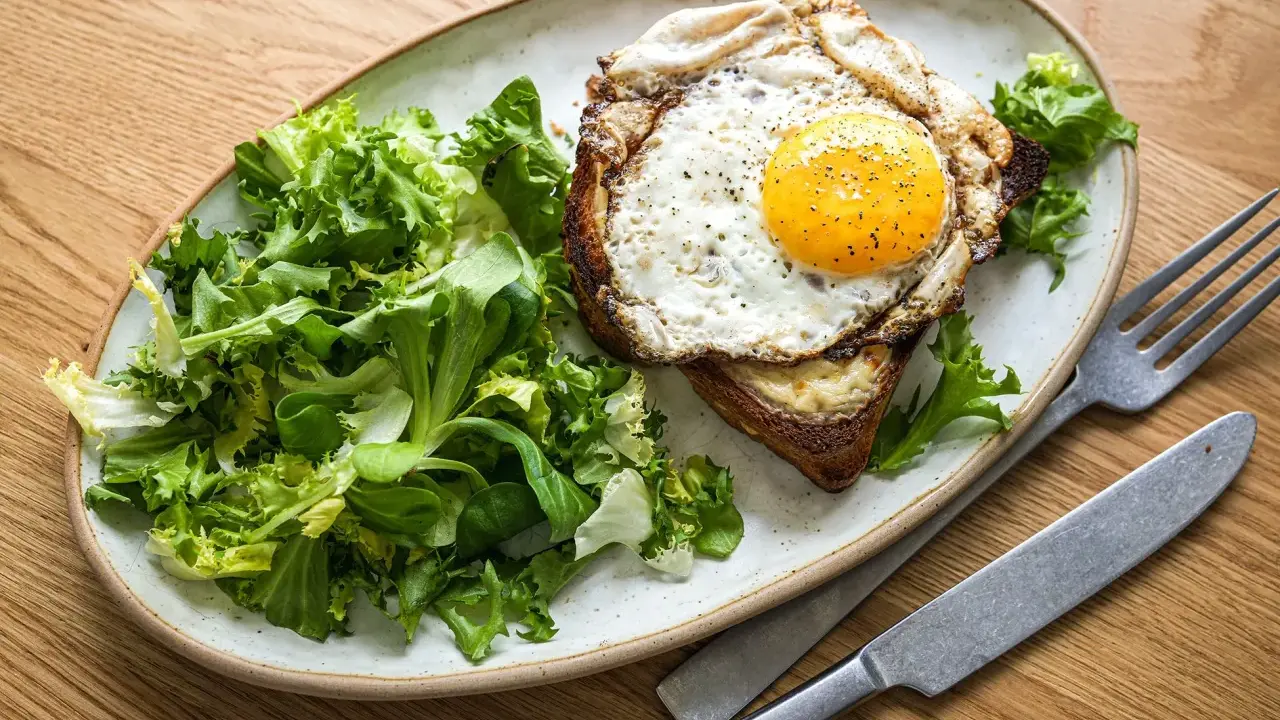 Ein Croque Madame mit Spiegelei, Käse und Toast, serviert mit frischem Salat.