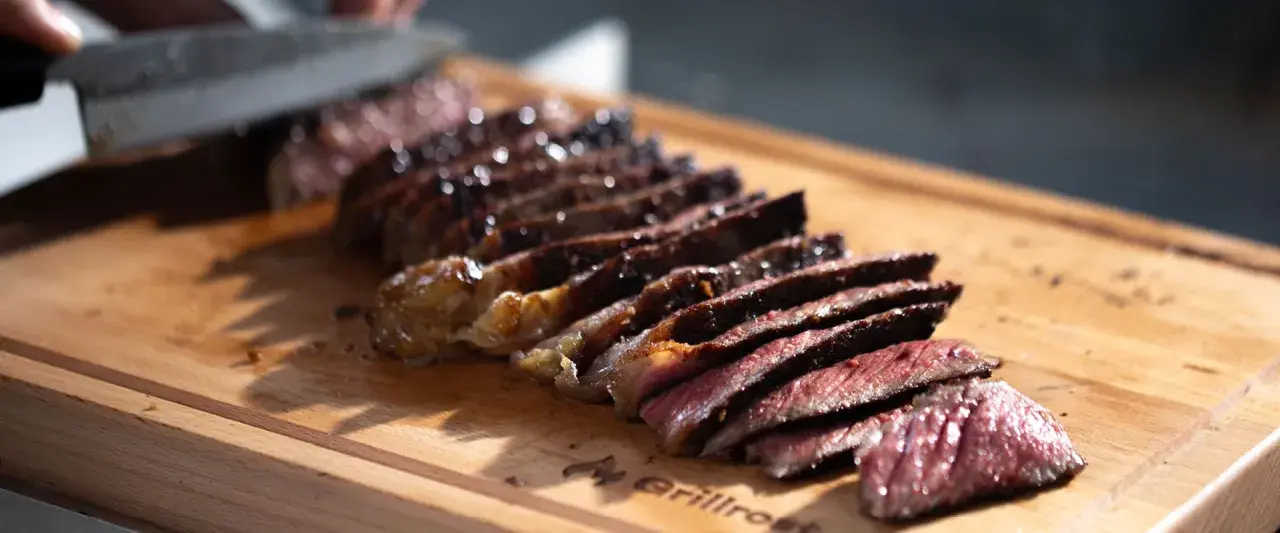 Saftiges Steak, auf einer Plancha zubereitet, wird auf einem Holzbrett in Scheiben geschnitten.