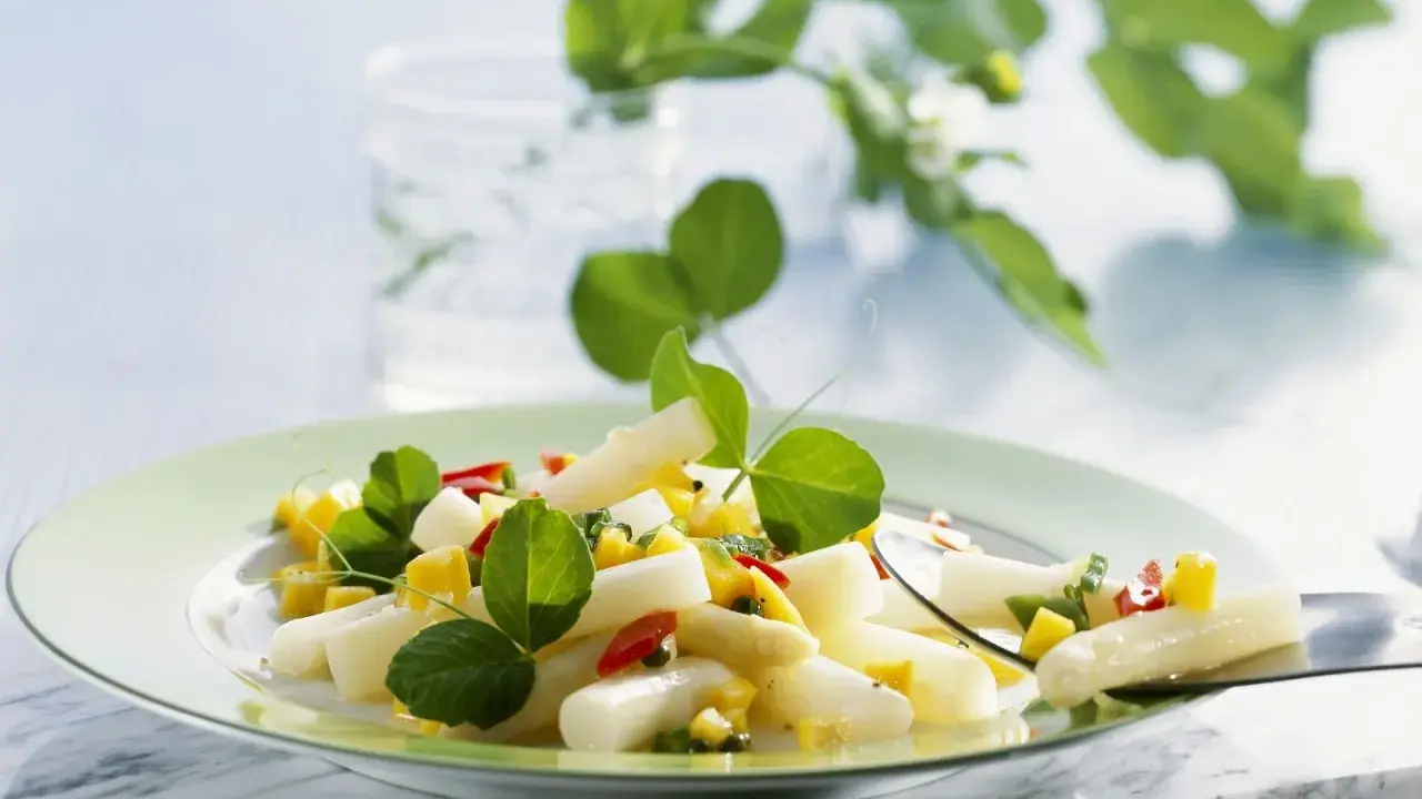 Ein frischer Spargel Mango Salat mit roten Paprikastückchen und grünen Blättern, garniert mit zarten Sprossen.