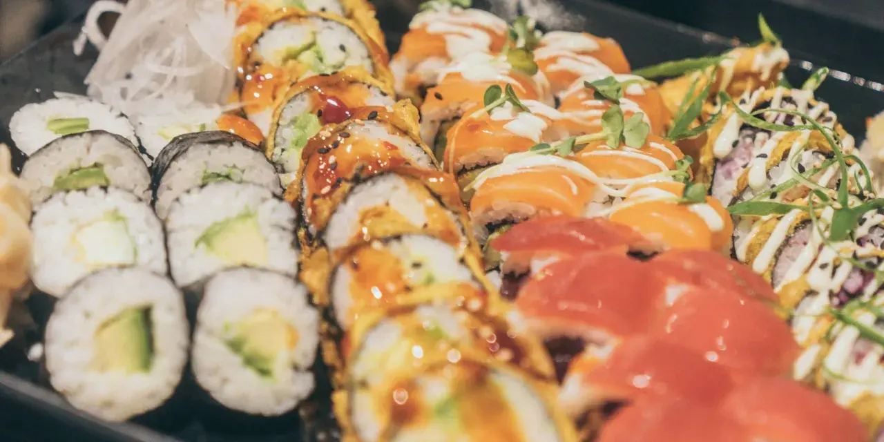 Vielfalt an Sushi-Rollen mit Lachs, Avocado und frischen Kräutern. Eine Frage, wie gesund ist Sushi, lässt sich hier nicht pauschal beantworten.
