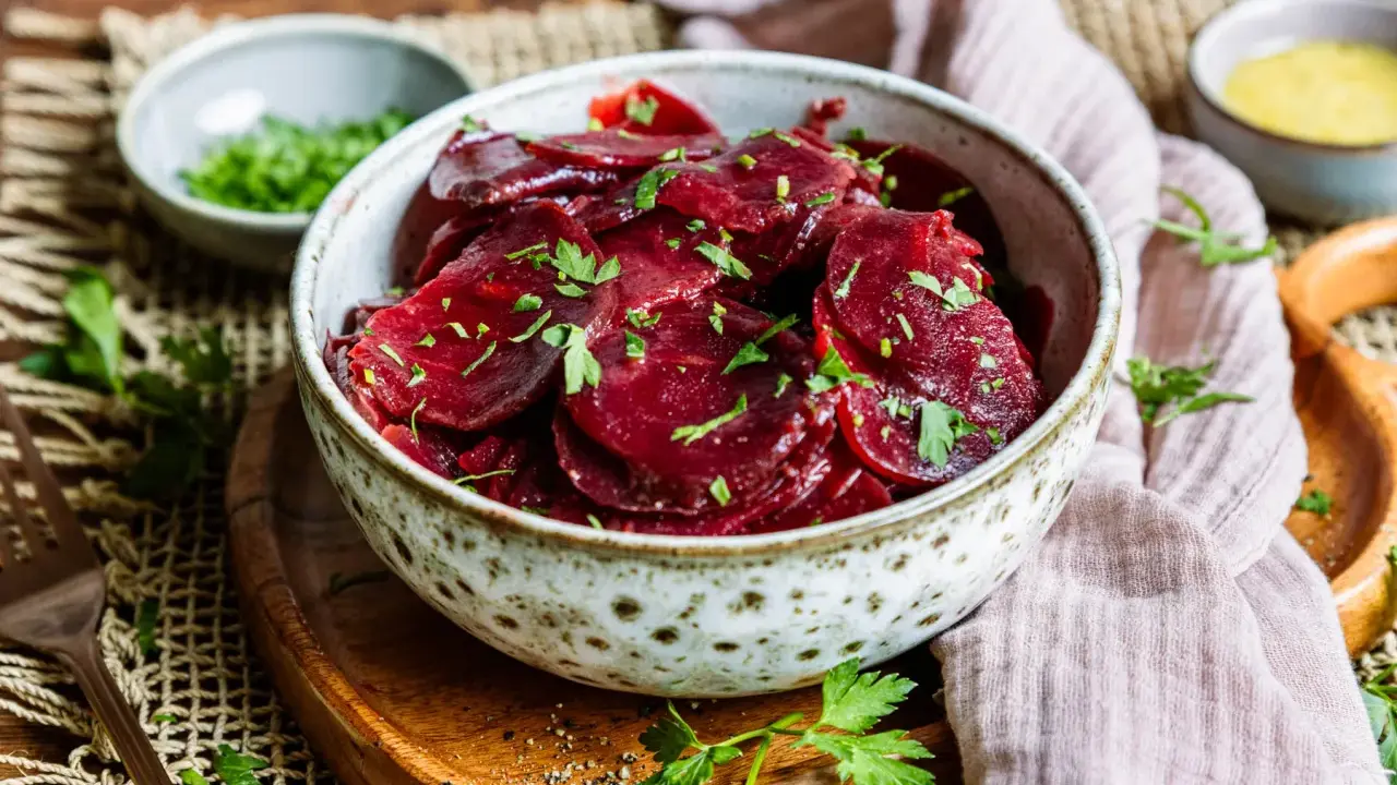 Schüssel mit traditionellem Rote Bete Salat, garniert mit Petersilie. Daneben kleine Schälchen mit Kräutern und Dressing.