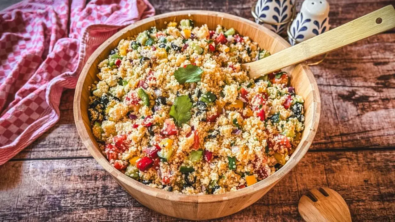 Ein bunter Couscous-Salat mediterran mit Tomaten, Gurken, Paprika und Oliven in einer Holzschüssel, bereit zum Servieren.