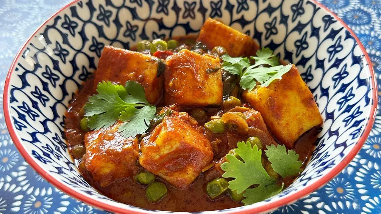 Schüssel mit cremigem Mattar Paneer, garniert mit Koriander. Die Sauce ist reichhaltig und rotbraun, mit Erbsen und würzigen Paneer-Würfeln.