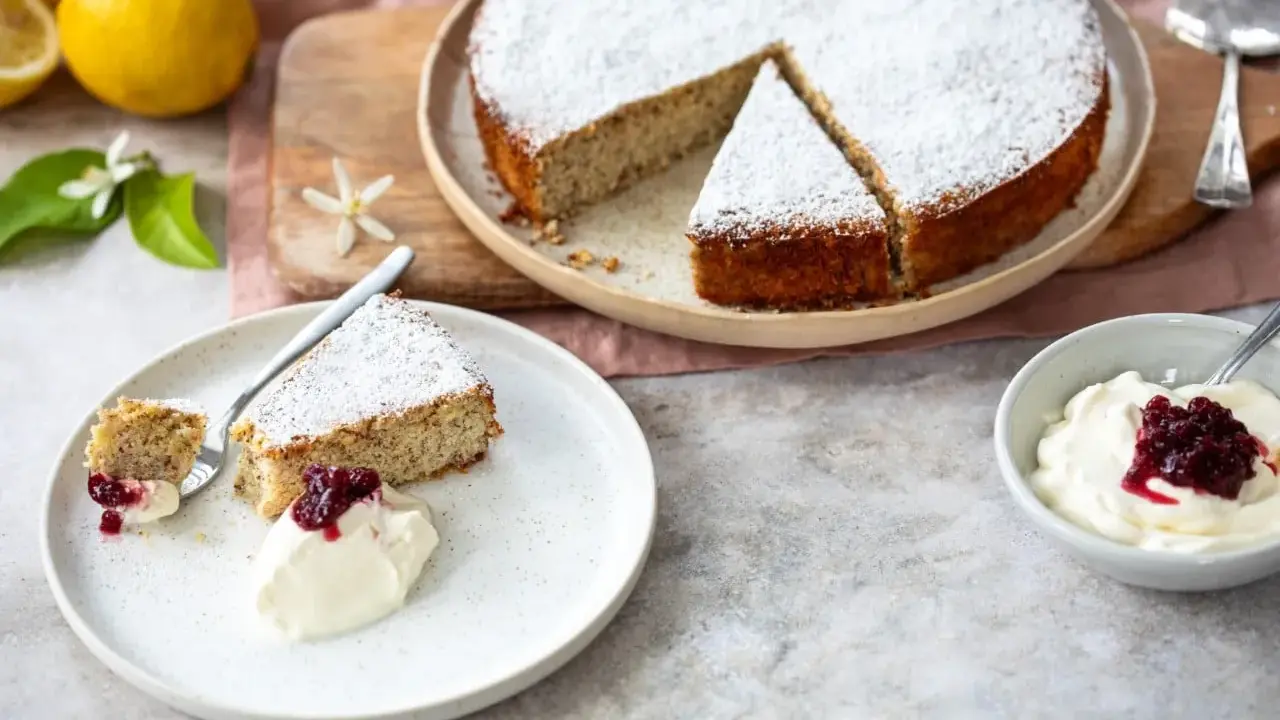 Ein saftiger Ricotta Mandel Kuchen, bestäubt mit Puderzucker, serviert mit einer Kugel Sahne und roter Grütze.