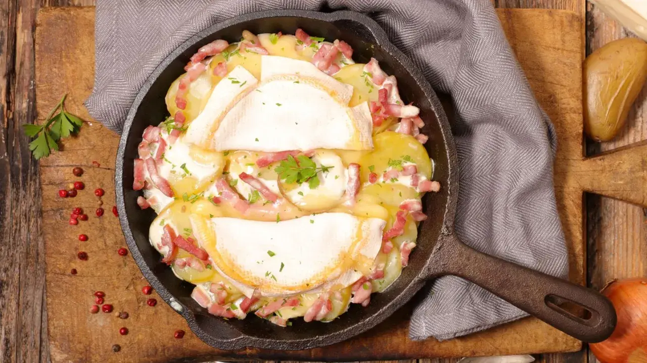 Herzhaftes Tartiflette-Rezept in Gusseisenpfanne: Kartoffeln, Speck und geschmolzener Käse, garniert mit Petersilie.