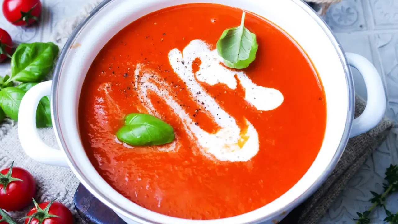 Eine cremige, beste Tomatensuppe mit Basilikum und einem Swirl Sahne, garniert mit frischen Tomaten und Kräutern.