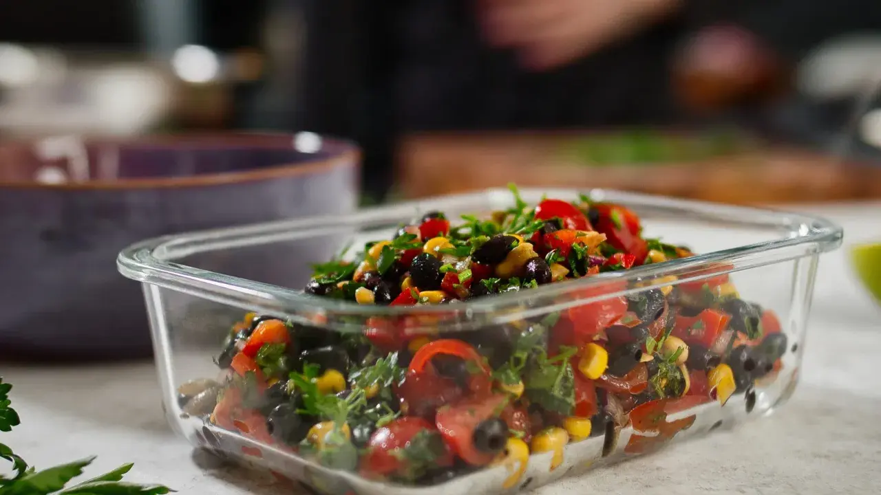 Frischer schwarze bohnen salat mit Mais, Tomaten und Kräutern in einer Glasbox, bereit zum Mitnehmen.
