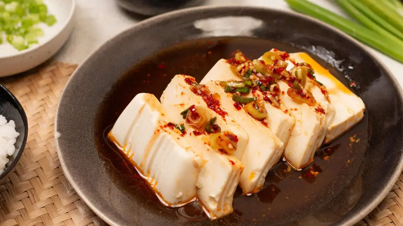 Seidiger Tofu, ein einfaches silken tofu recipe, serviert mit Frühlingszwiebeln und Chili-Öl auf einem dunklen Teller.