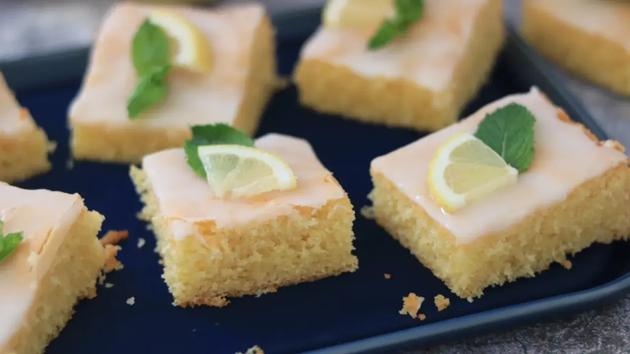 Saftige Kuchenstücke mit Zitronenguss, garniert mit Zitronenspalten und Minze. Ein Genuss, der nach dem besten zitronenkuchen der welt schmeckt.