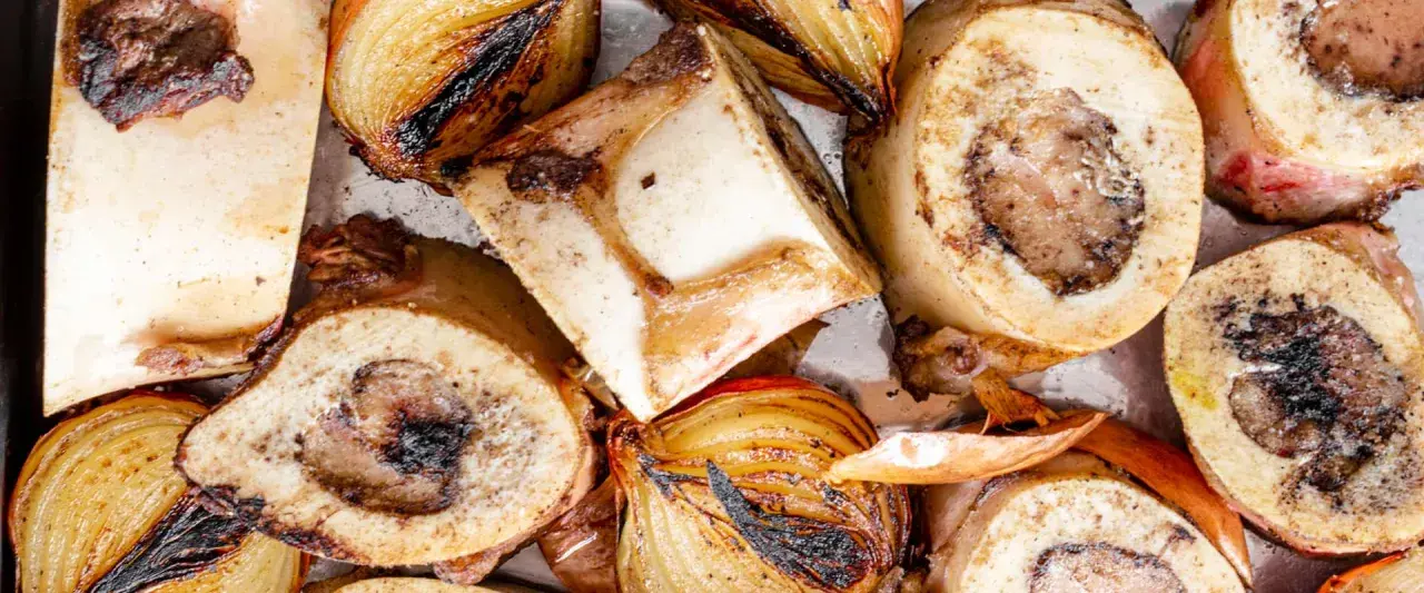 Rinderknochen auskochen Rezept: Geröstete Rinderknochen und Zwiebeln auf einem Blech, bereit für eine herzhafte Brühe.