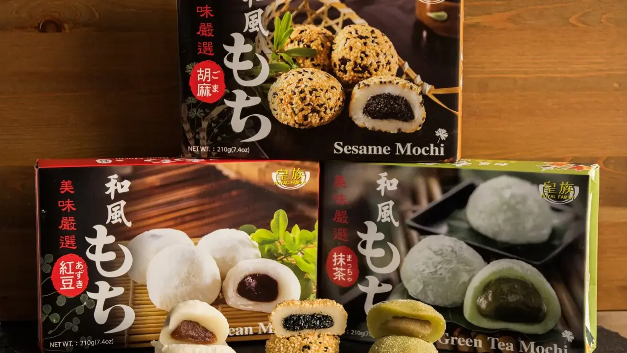 Verschiedene Sorten japanischer Reiskuchen (Mochi) mit Sesam, roter Bohne und grünem Tee, auf dunklem Untergrund vor Holz.
