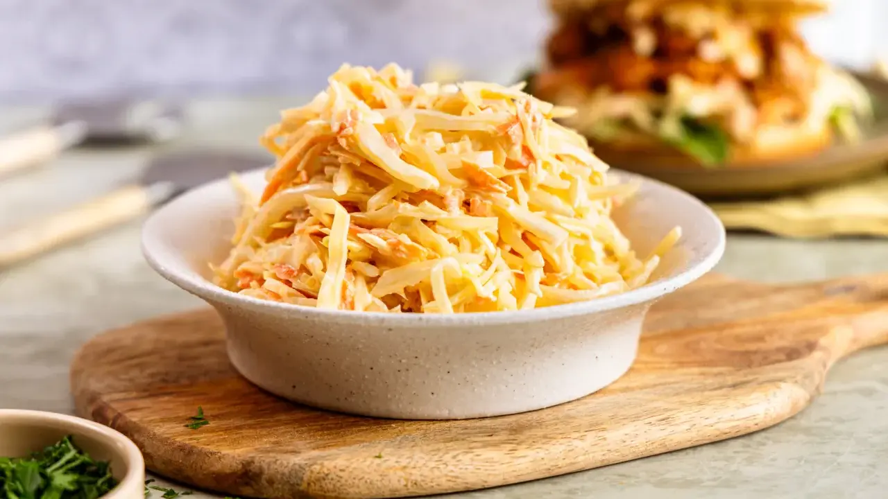 Schüssel mit cremigem Coleslaw, perfekt für das **rezept coleslaw original**. Im Hintergrund ein Burger.