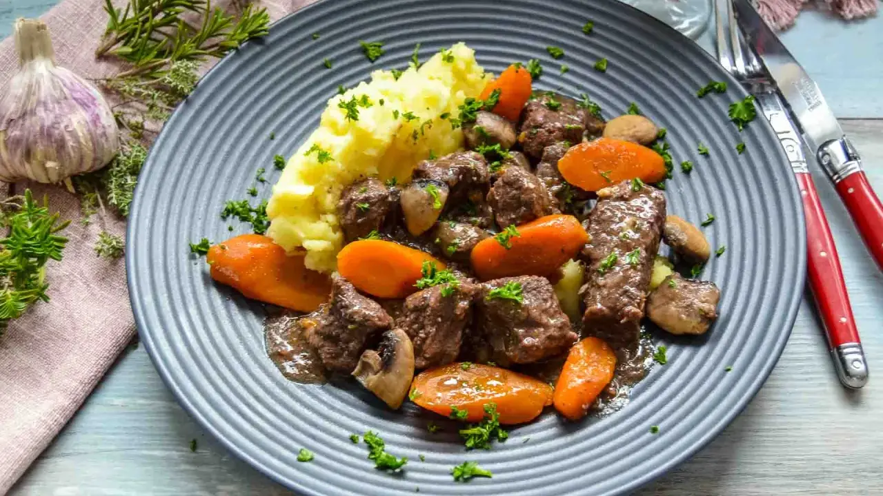 Herzhaftes Boeuf Bourguignon Rezept mit zartem Rindfleisch, Karotten, Pilzen und Kartoffelpüree, garniert mit Petersilie.