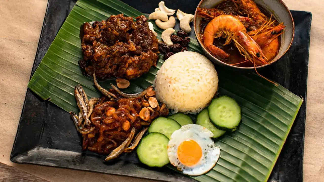 Nasi Lemak: Reis, scharfe Garnelen, frittierte Sardellen, Spiegelei, Gurkenscheiben, Cashewkerne und Rosinen auf Bananenblatt.