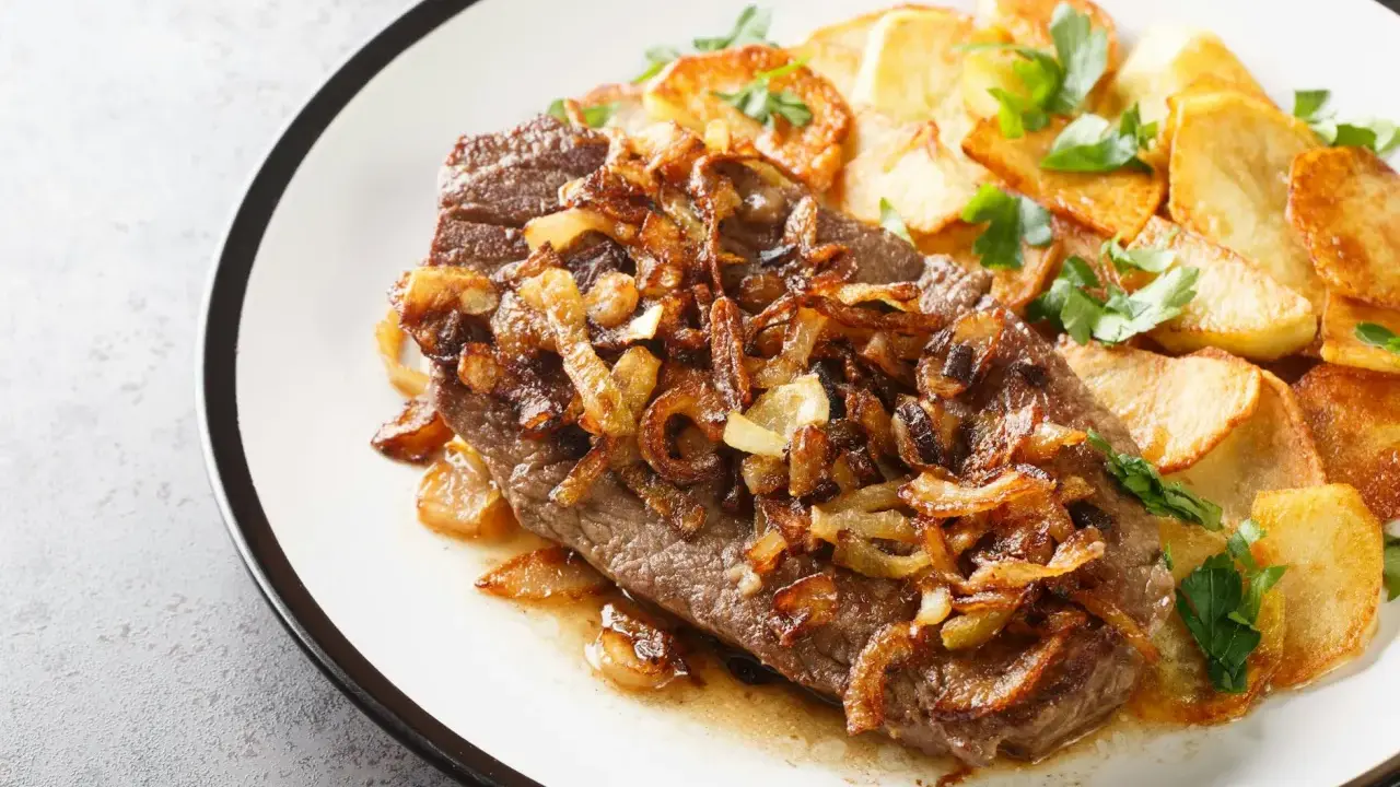 Ein saftiges Stück Rindfleisch, bedeckt mit goldbraunen Röstzwiebeln, serviert mit knusprigen Bratkartoffeln. Das ist der beste Zwiebelrostbraten!