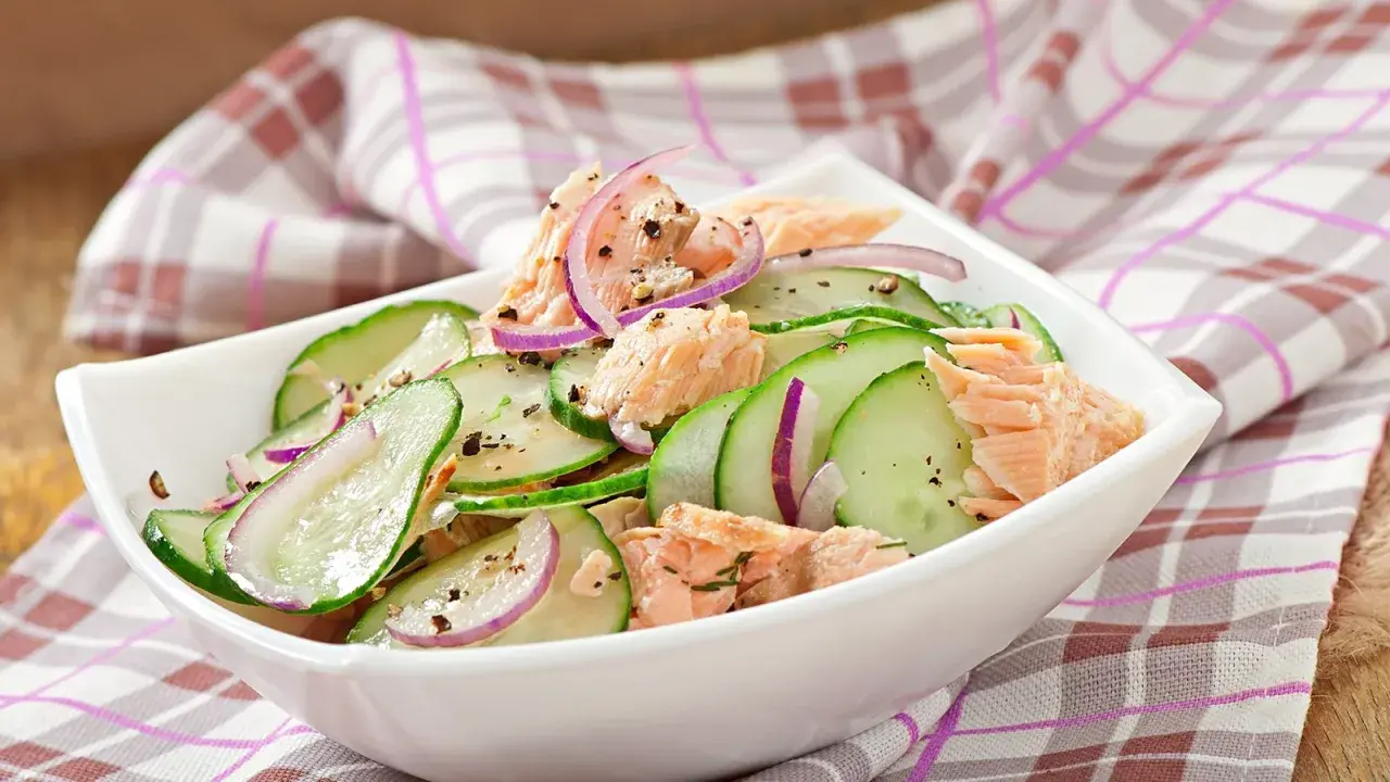 Frischer Gurkensalat mit zarten Lachsstücken und roten Zwiebelringen, gewürzt mit Pfeffer. Ein leichter und gesunder Salat.