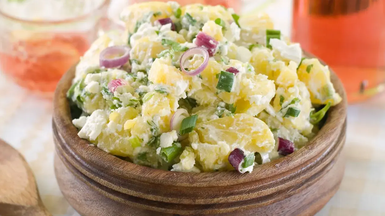Herzhafter Kartoffelsalat mit Meerrettich, verfeinert mit Frühlingszwiebeln und roten Zwiebelringen, serviert in einer Holzschale.