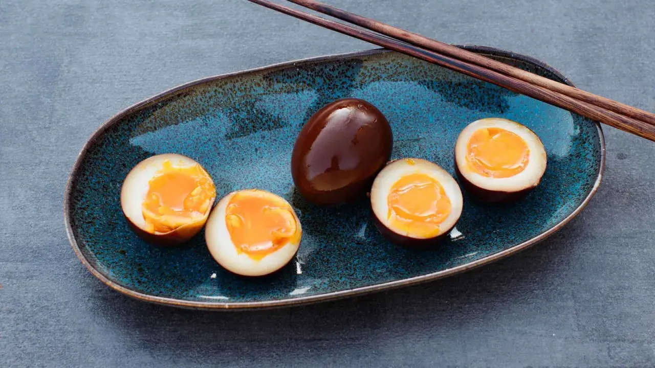 Dunkelbraune, marinierte Ramen-Eier auf einem blauen Teller, drei davon halbiert, mit flüssigem Eigelb.
