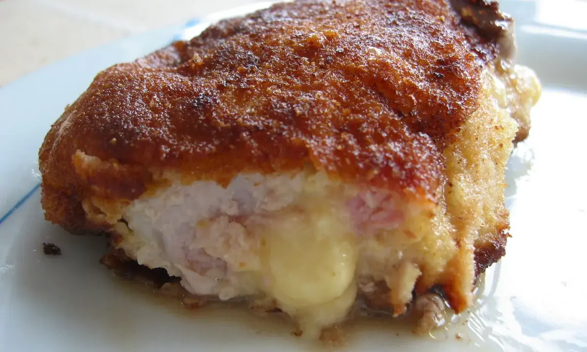 Ein goldbraunes Cordon Bleu, das innen mit geschmolzenem Käse und Schinken gefüllt ist. Seine Herkunft ist oft umstritten, aber der Geschmack ist unbestritten.