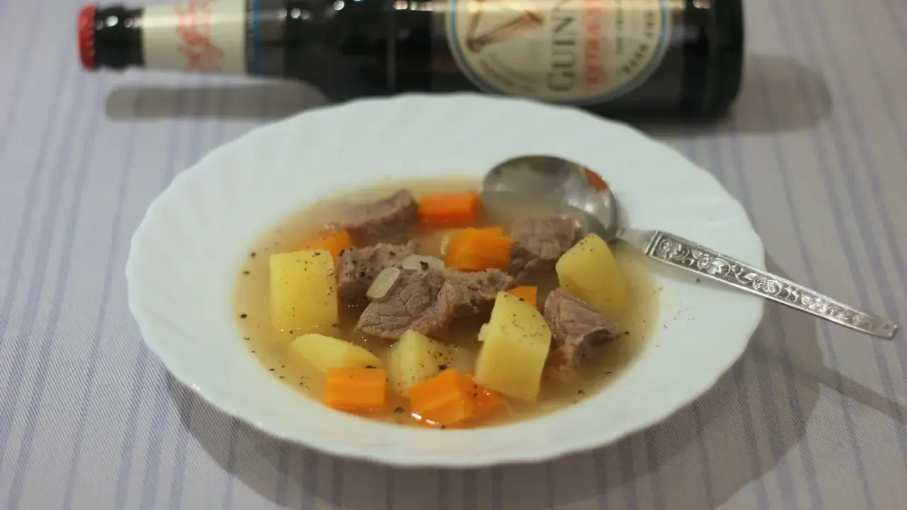 Herzhafter Irish Stew mit Kartoffeln und Karotten in einer Schüssel, daneben eine Flasche Guinness.