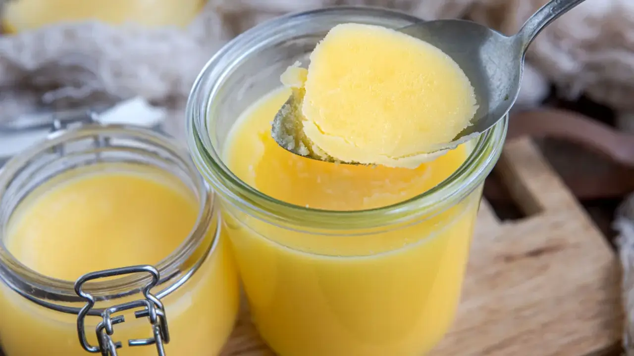 Ein Löffel Butterschmalz wird aus einem Glas gehoben. Dieses goldgelbe Fett ist ideal zum Braten, da sein hoher Butterschmalz rauchpunkt Verbrennungen verhindert.