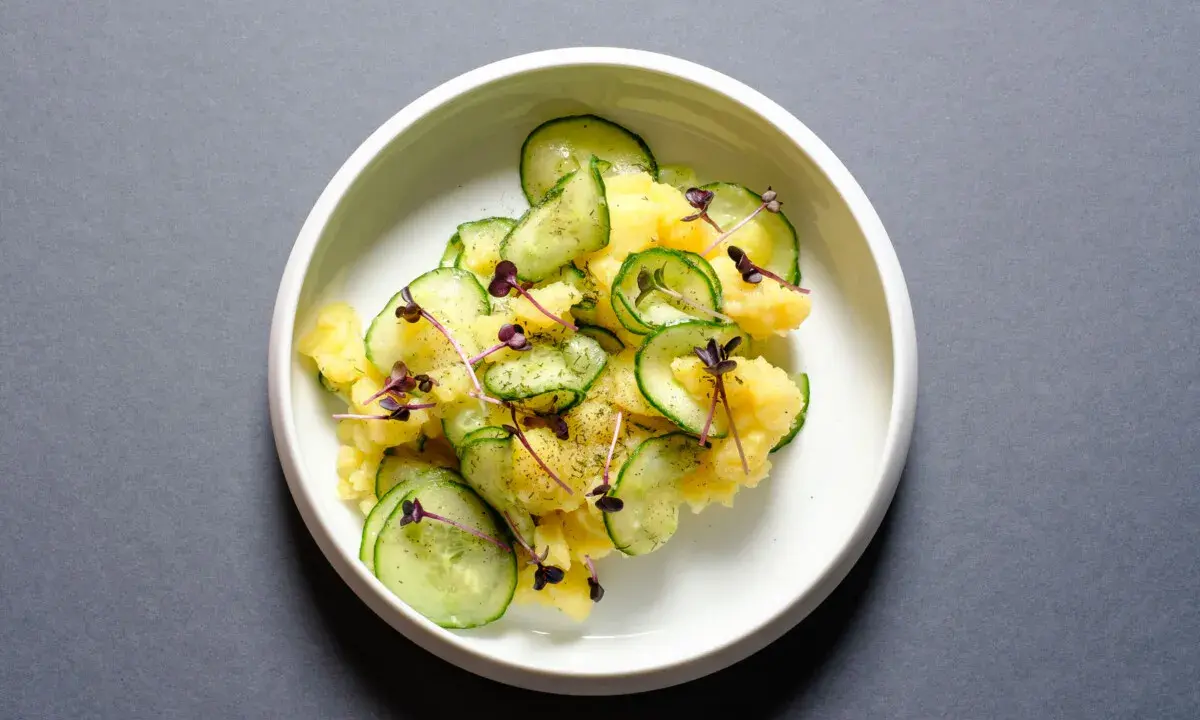Kartoffelsalat mit frischer Gurke, garniert mit lila Sprossen und Dill. Ein leichter und erfrischender Genuss.