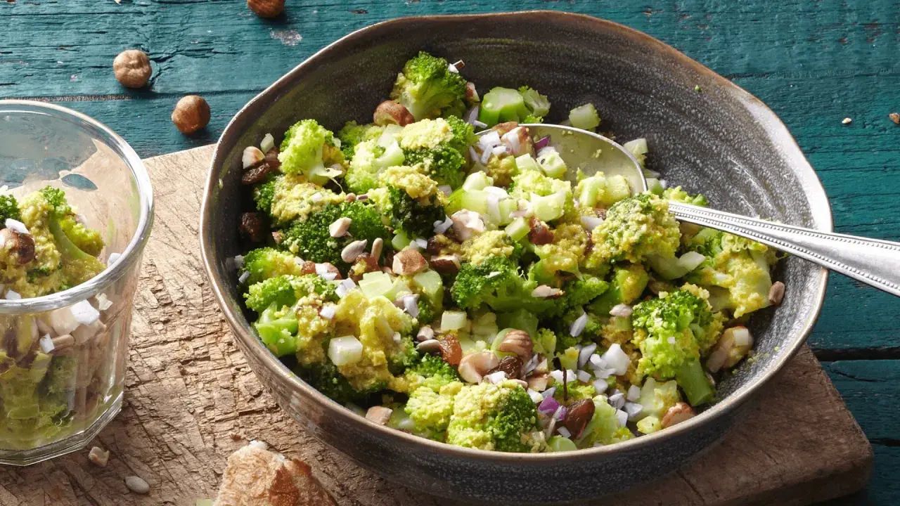 Ein einfacher Brokkoli-Salat mit Nüssen und Rosinen, serviert in einer Schüssel auf einem Holztisch.