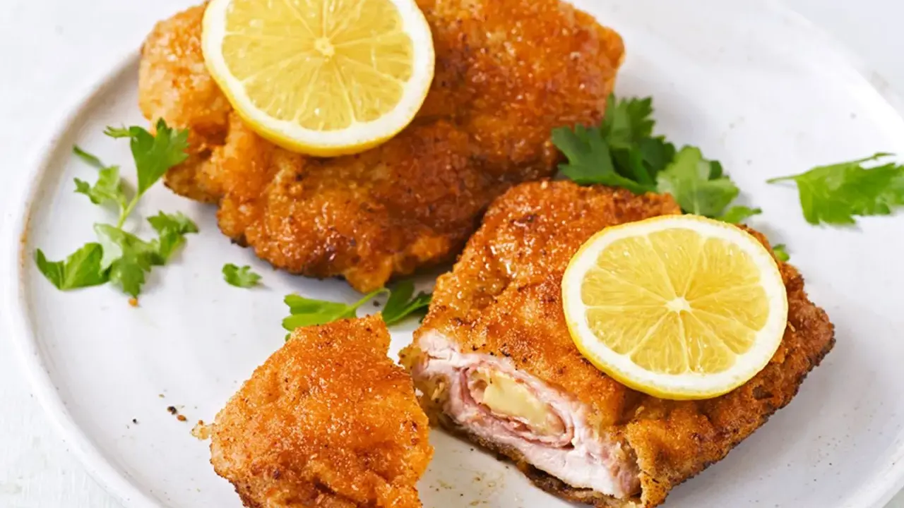 Zwei goldbraune Cordon Bleu mit geschmolzenem Käse und Schinken, garniert mit Zitronenscheiben und Petersilie.