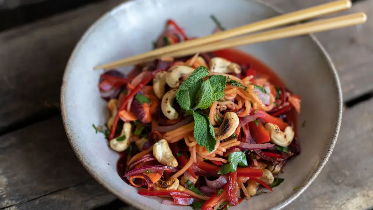 Bunter Papaya-Salat mit reifer Papaya, Karottenstreifen, Cashewkernen und Minze, serviert mit Stäbchen.