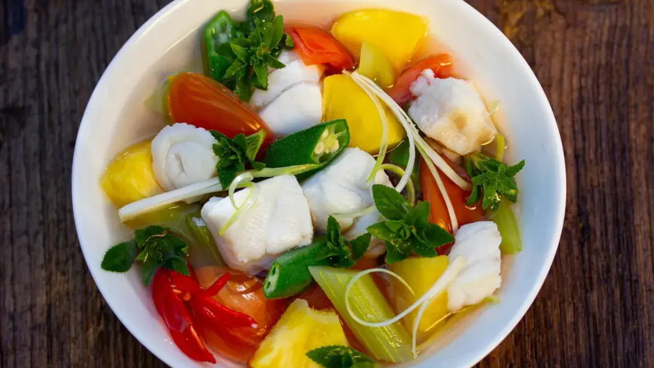 Ein Schüssel mit Canh Chua, einem vietnamesischen Fisch-Gemüse-Eintopf, mit Ananas, Tomaten, Okra und Kräutern.