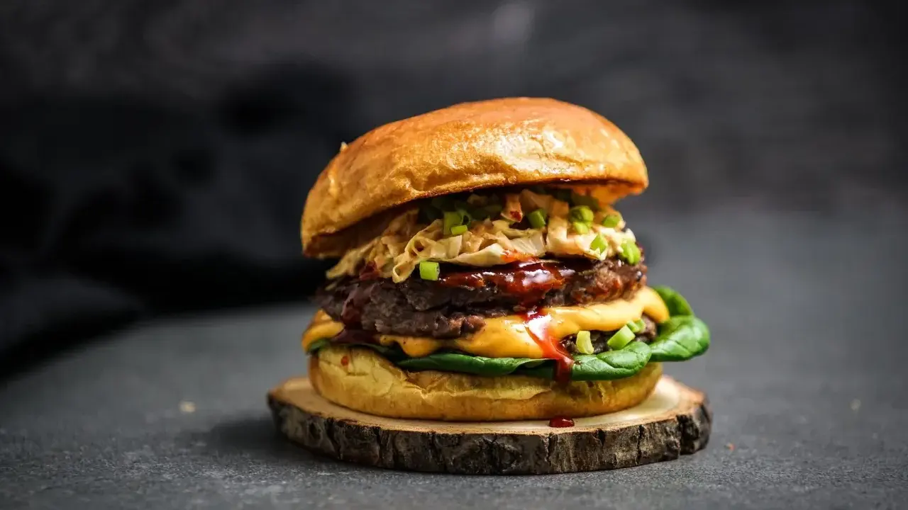Ein saftiger koreanischer Burger mit doppeltem Patty, Käse, knackigem Krautsalat und Frühlingszwiebeln auf einem rustikalen Holzbrett.