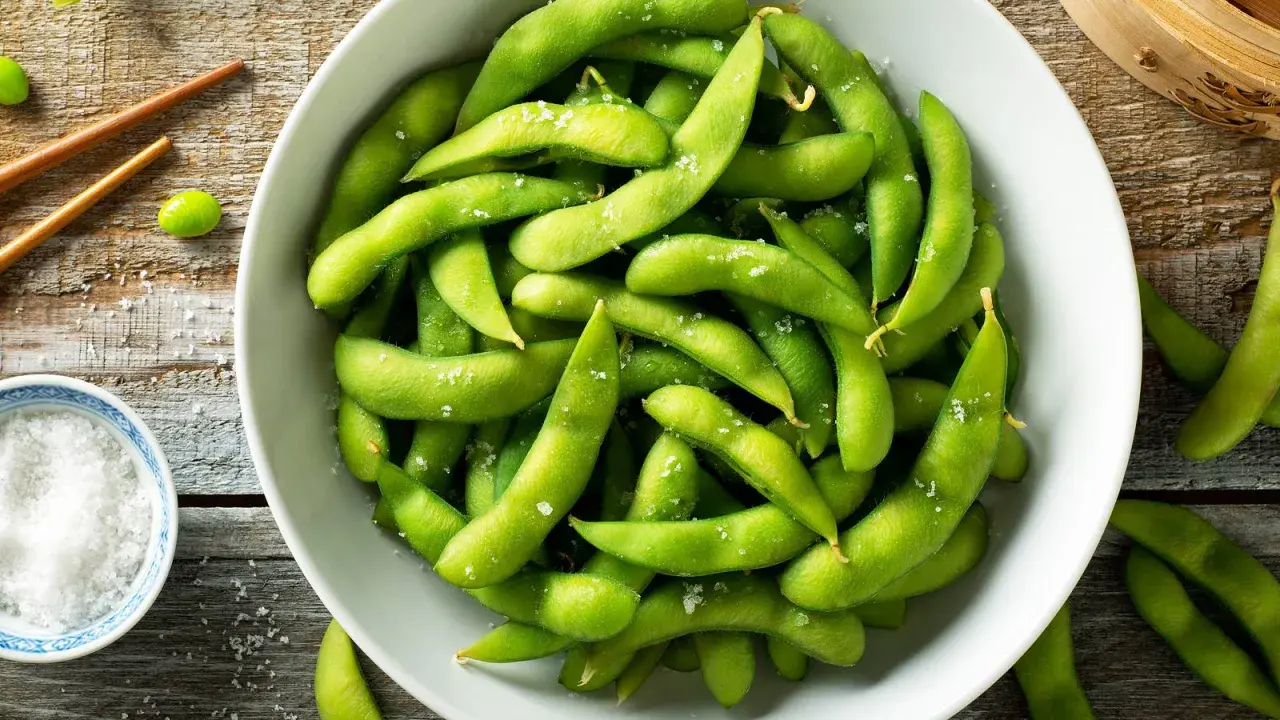 Salzige Edamame-Schoten in einer Schüssel, bereit zum Genießen. So isst man Edamame: die Schote aufbeißen und die Bohnen herausdrücken.