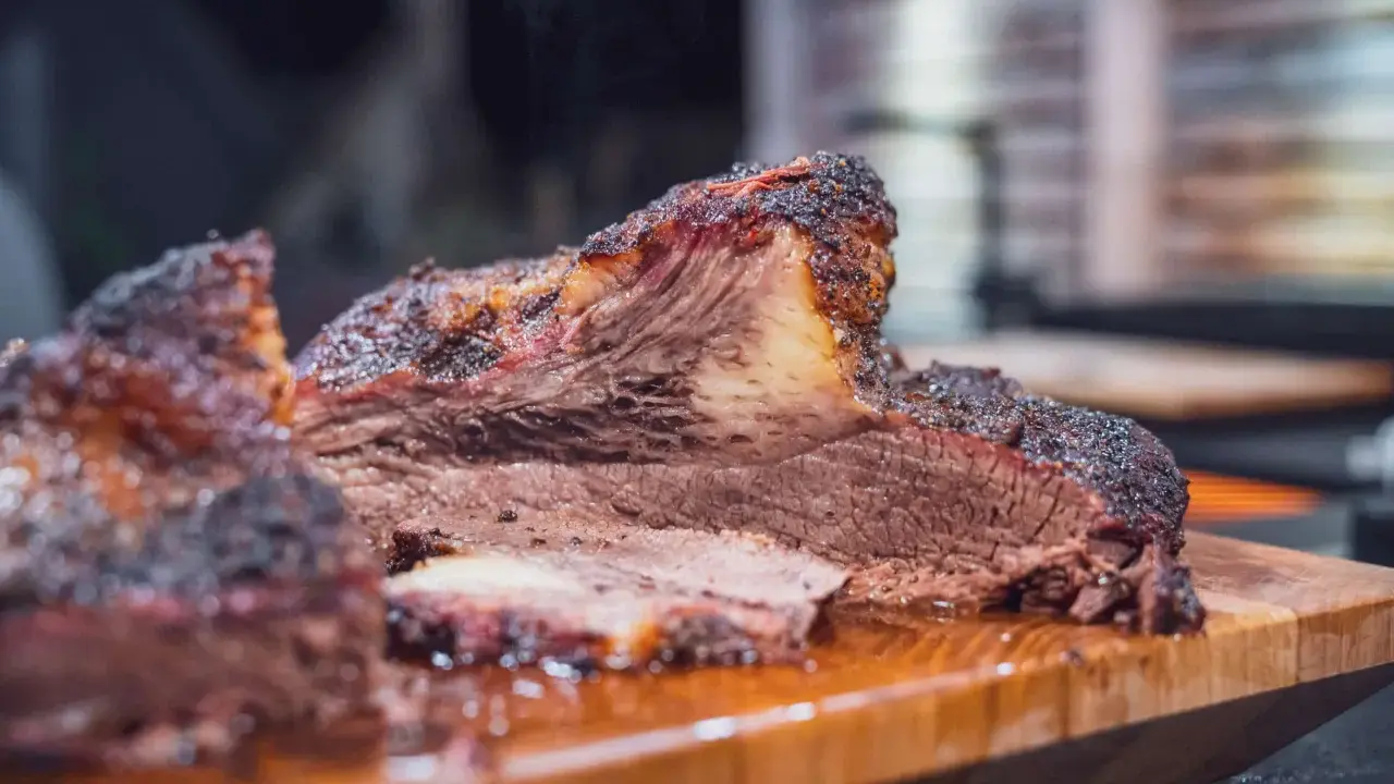 Saftiges Rind Brisket mit dunkler Kruste, auf einem Holzbrett serviert. Der Rauch steigt auf und verspricht ein zartes Geschmackserlebnis.
