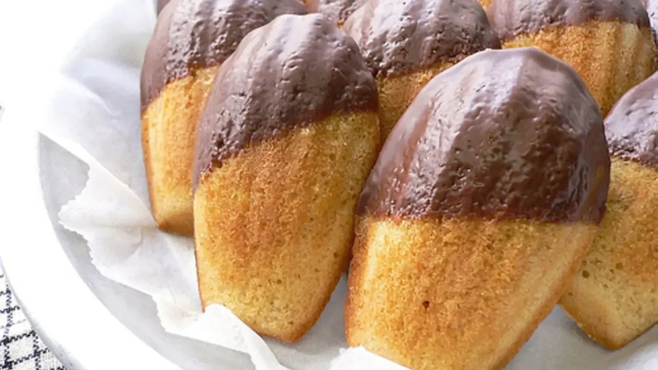 Eine Reihe von Madeleines, die zur Hälfte in Schokolade getaucht sind, warten darauf, gegessen zu werden.