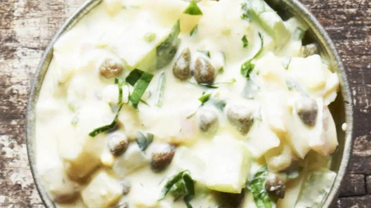 Cremiger Kartoffelsalat mit Kapern und frischen Kräutern, serviert in einer Metallschale auf rustikalem Holz.