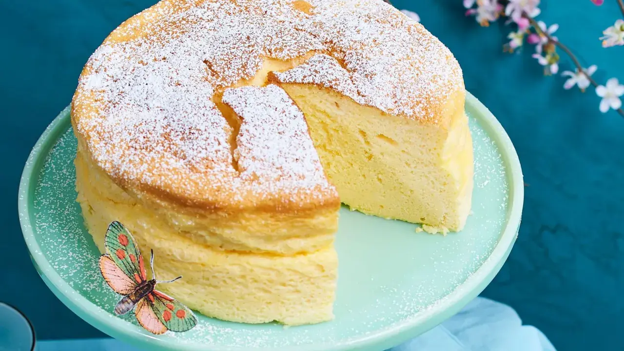Ein luftiger, japanischer Kuchen, bestäubt mit Puderzucker, steht auf einem mintgrünen Tortenständer. Ein Schmetterling sitzt am Rand.