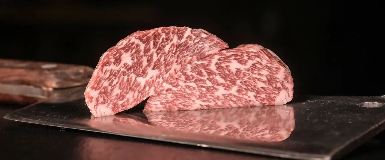 Zwei saftige Steaks vom Kobe Rind liegen auf einem metallischen Untergrund. Ihr auffälliges Marmormuster aus Fett und Fleisch verspricht ein einzigartiges Geschmackserlebnis.