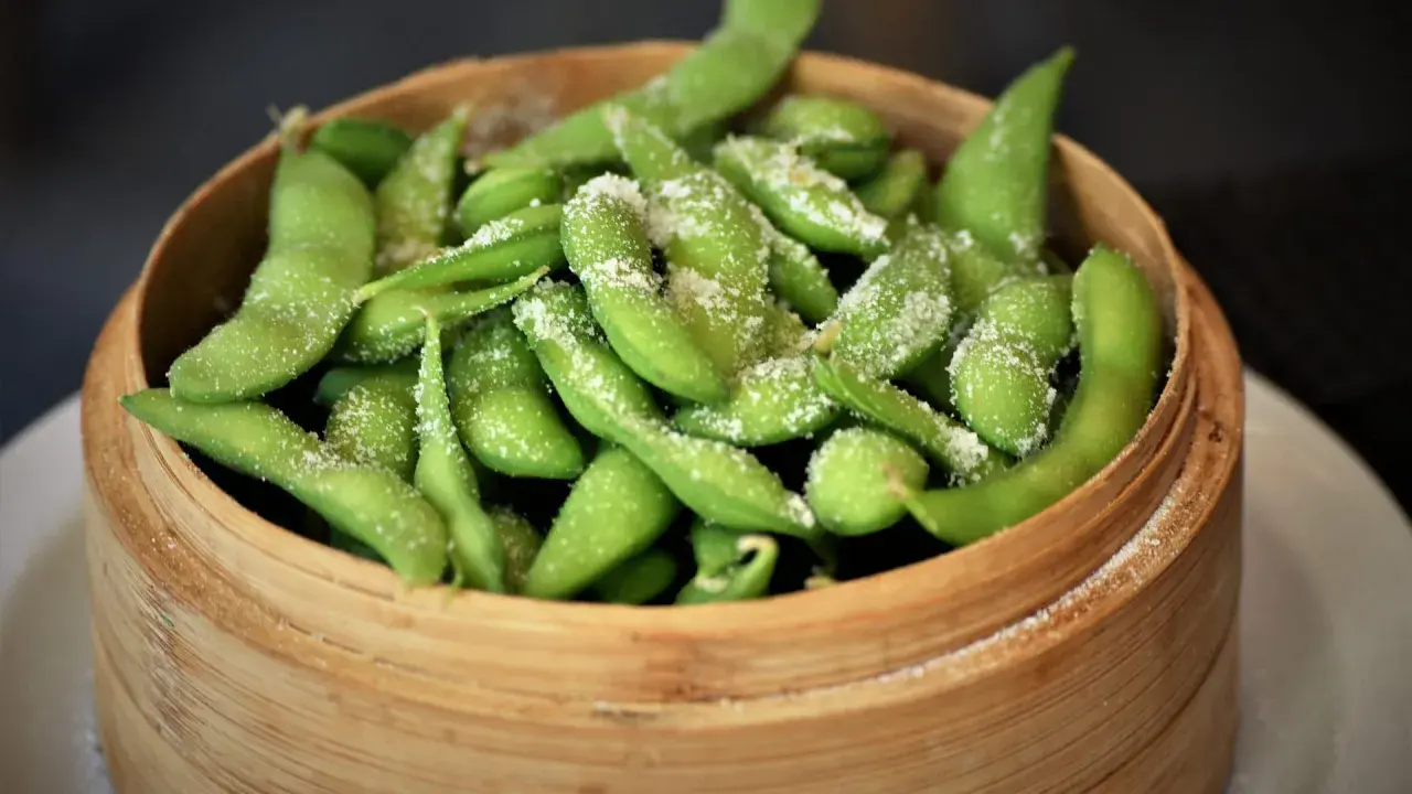 Frische Edamame-Schoten, leicht gesalzen, bereit zum rohen Essen. Ein gesunder Snack in einem Bambuskorb.