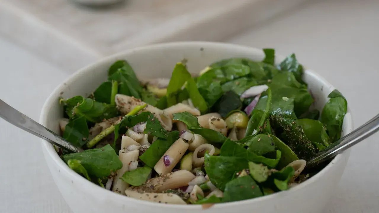 Ein frischer nudelsalat mit spargel, garniert mit Spinat und roten Zwiebeln, bereit zum Genießen.