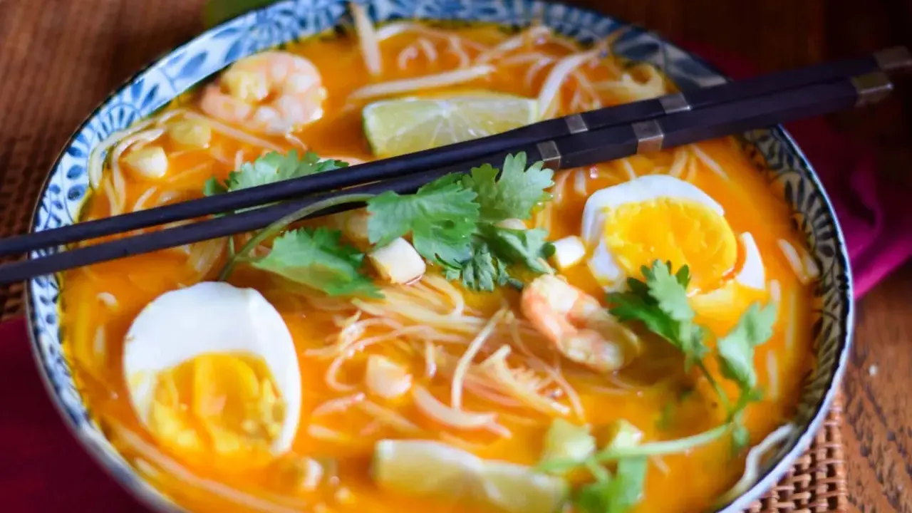 Eine Schüssel mit köstlicher Laksa Suppe, garniert mit Garnelen, Ei, Limette und Koriander.