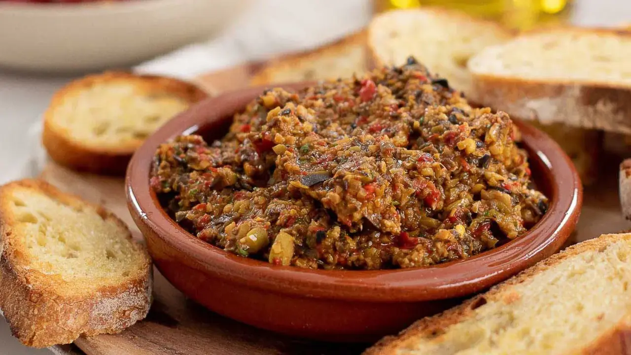 Herzhafte Tapenade deutsch in einer Tonschale, umgeben von geröstetem Brot. Ein Genuss für jeden Feinschmecker.