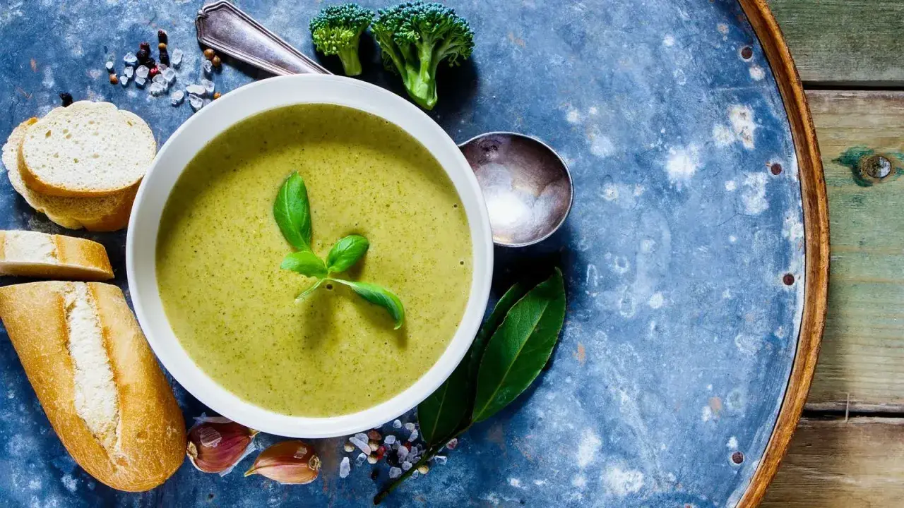 Grüne Detox-Suppe mit frischem Basilikum, dazu Baguettescheiben, Knoblauch und Brokkoli.