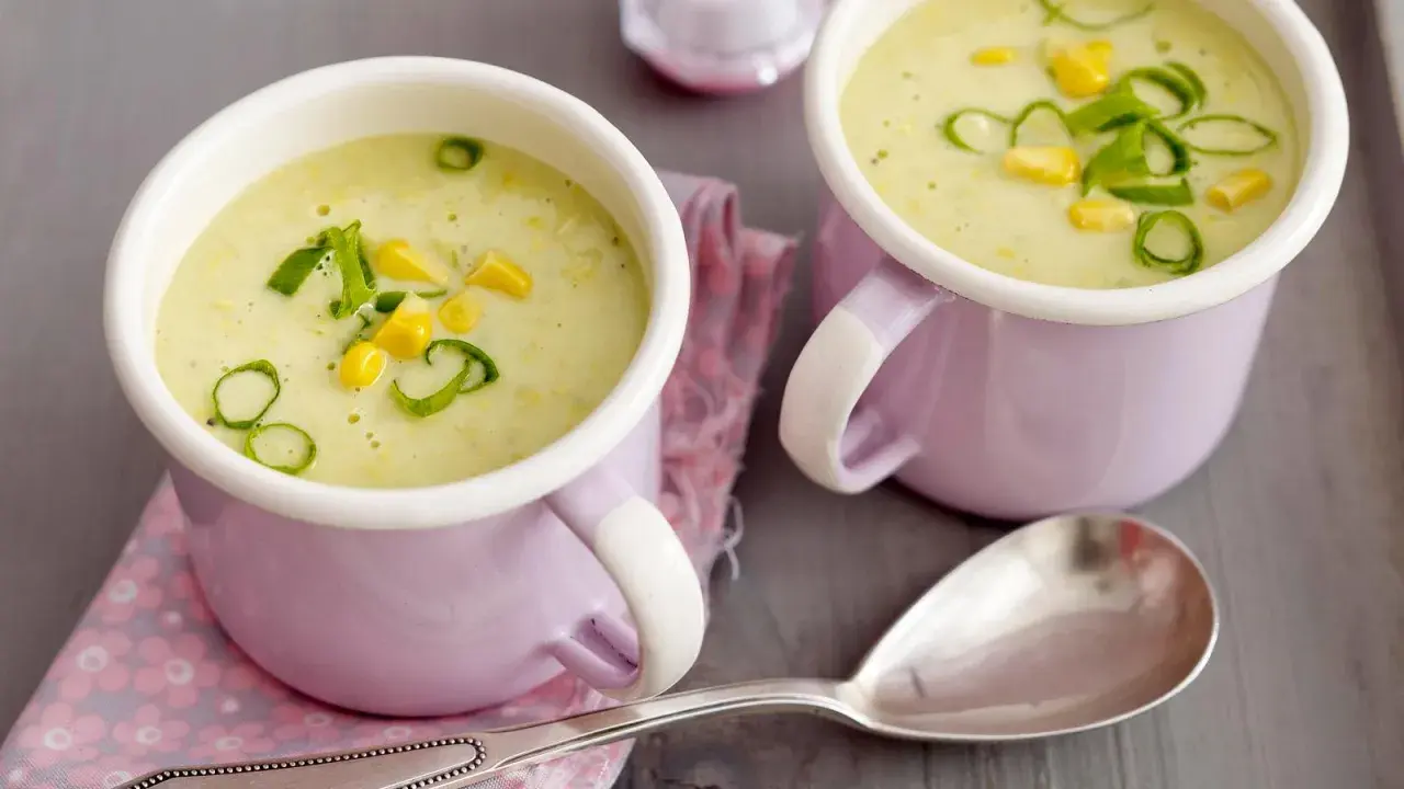 Zwei Tassen cremiger Maissuppe mit Kokosmilch, garniert mit Maiskörnern und Frühlingszwiebeln.