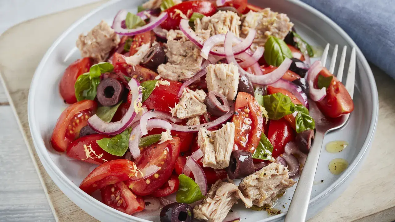 Frischer Tomaten-Thunfisch-Salat mit roten Zwiebeln und Oliven, garniert mit Basilikum. Ein leichter und gesunder Genuss.