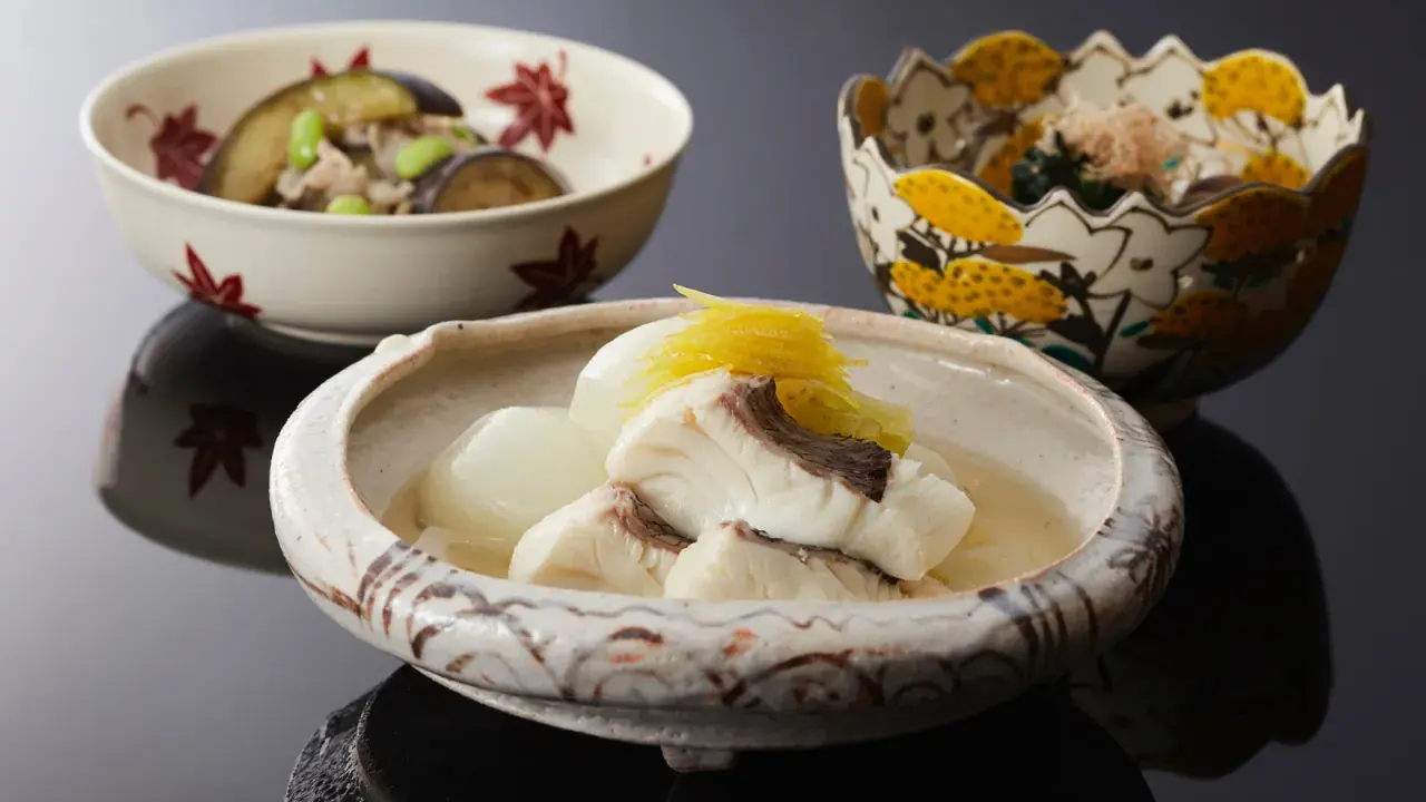 Drei Schalen mit japanischem Essen. Eine Schale enthält Fisch in Brühe, was ist dashi. Eine weitere Schale mit Auberginen und Edamame.