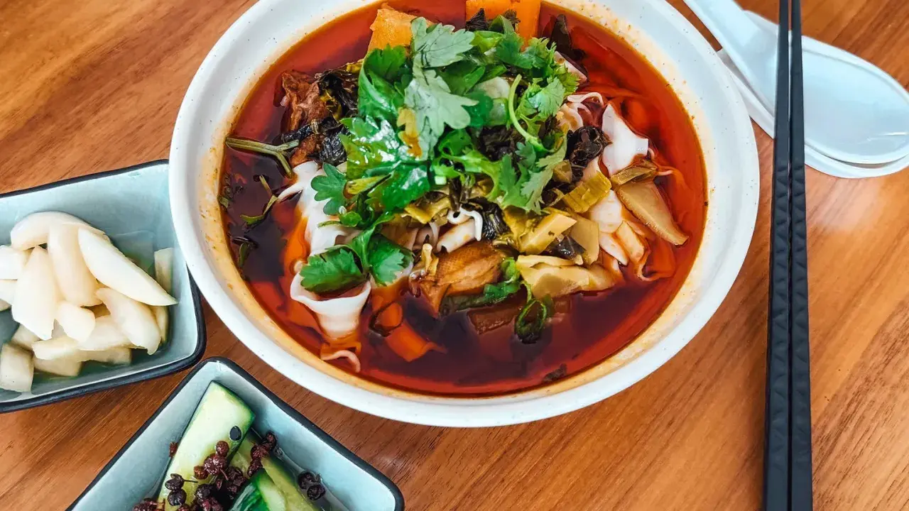Eine Schüssel mit aromatischer taiwanischer Rindernudelsuppe, garniert mit frischem Koriander, daneben eingelegte Gurken und Rettich.