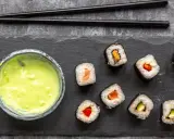 Sushi mit Lachs, Avocado und Paprika, dazu eine grüne Soße. Ist Wasabi gesund? Ja, es ist bekannt für seine entzündungshemmenden Eigenschaften.