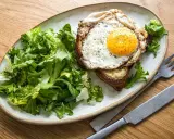 Ein Croque Madame mit Spiegelei, Käse und Toast, serviert mit frischem Salat.
